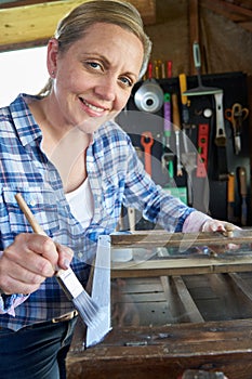 Portrait Of Mature Woman Upcycling Furniture In Workshop At Home Painting Cabinet