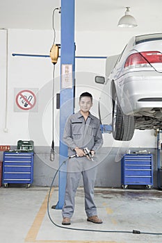 Portrait of Mechanic with Power Tool Next to Car Wheel, Looking At Camera