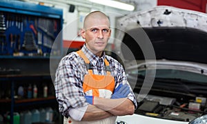 Portrait of mechanician posing near car at auto service