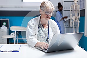 Portrait of medic with stethoscope using laptop to work on healthcare in cabinet