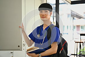 Portrait of medical student man wearing blue scrubs with stethoscope standing near window at campus