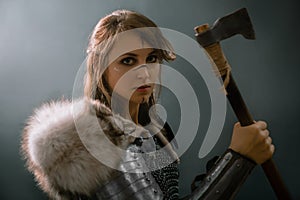 Portrait of a medieval fantasy female warrior in armor armed with an ax, posing in the studio in the dark on a black background
