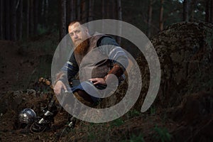 Portrait of medieval red-haired viking warrior with beard with an ax in forest