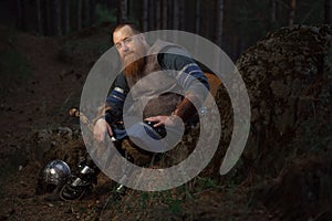 Portrait of medieval red-haired viking warrior with beard with an ax in forest