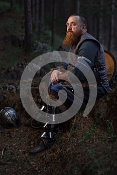 Portrait of medieval red-haired viking warrior with beard with an ax in forest