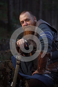Portrait of medieval red-haired viking warrior with beard with an ax in forest