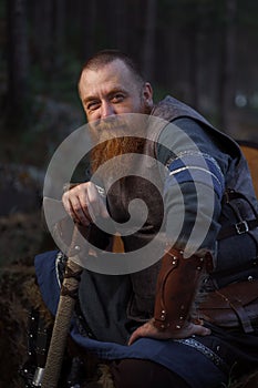 Portrait of medieval red-haired viking warrior with beard with an ax in forest