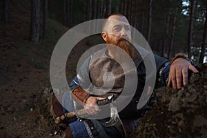 Portrait of medieval red-haired viking warrior with beard with an ax in forest