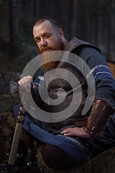 Portrait of medieval red-haired viking warrior with beard with an ax in forest