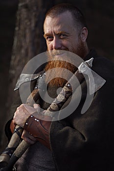 Portrait of medieval red-haired viking warrior with beard with two axes