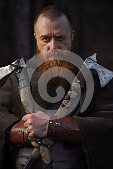 Portrait of medieval red-haired viking warrior with beard with two axes