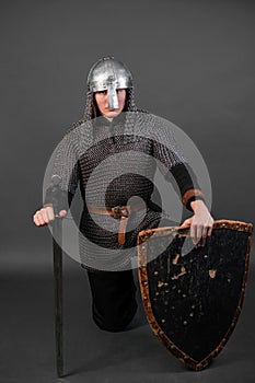 Portrait of a medieval warrior of the late viking era and the beginning of the crusades sitting on his knee. Knight in chain mail