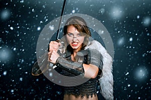 Portrait of a medieval woman warrior in chain mail and fur with a sword in her hands posing while standing in a snowstorm.