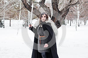 Portrait of a medieval woman, warrior of the Viking Age in the winter forest on the background of a large tree.