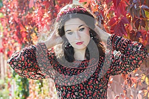 Portrait of melancholy autumn girl with autumn wreath at red floral background of grape woodbine photo