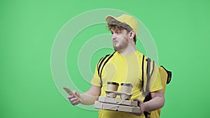Portrait of men holding coffee and pizza, specifying delivery address using smartphone. Male in yellow courier uniform