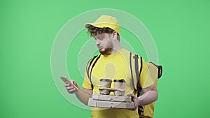 Portrait of men holding coffee and pizza, specifying delivery address using smartphone. Male in yellow courier uniform