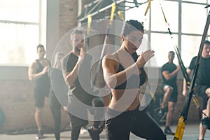 Portrait of men and women doing fitness training exercises at industrial gym. Straps, group workout concept