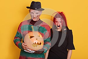 Portrait of man and woman with halloween pumpkin against yellow studio background, male with knives instead of fingers and female