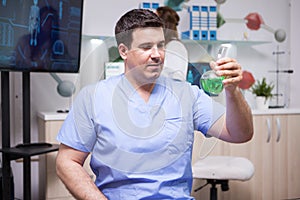 Portrait of microbiologist man holding a test tube with green solution in scientific laboratory