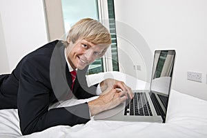 Portrait of mid adult businessman using laptop in bed at home