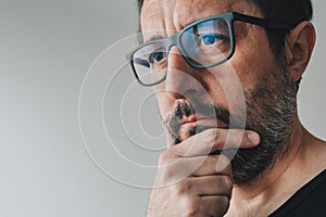 Portrait of mid-adult contemplative man with eyeglasses, man thinking and holding chin