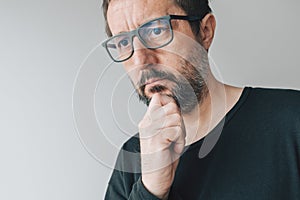 Portrait of mid-adult contemplative man with eyeglasses, man thinking and holding chin