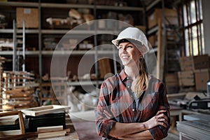 Portrait of mid-adult female carpenter standing in carpentery workshop, looking aside and smiling. Small business