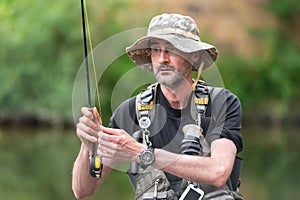 Portrait of mid adult fisherman on river, relaxing and fishing trouts.