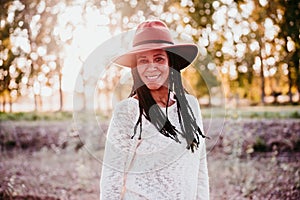 Portrait of mid adult hispanic woman wearing a hat at sunset during golden hour, autumn season