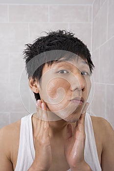 Portrait of mid adult man applying aftershave lotion in bathroom