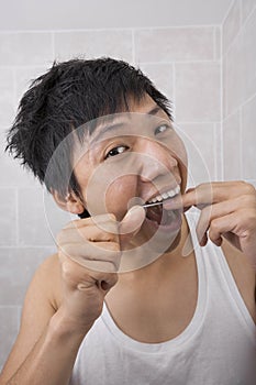 Portrait of mid adult man flossing his teeth in bathroom