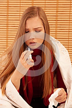 Portrait of a mid adult woman holding a bottle of nasal spray and suffering from cold