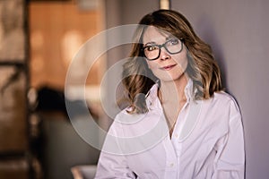 Portrait of mid aged woman wearing white shirt and standing at wall