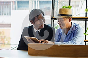 Portrait middle age businessman discussing something positive with his freind and showing something in tablet at coffee shop