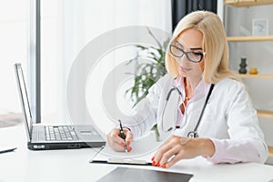 Portrait of middle age female doctor is wearing a white doctor& x27;s coat with a stethoscope around her neck. Smiling