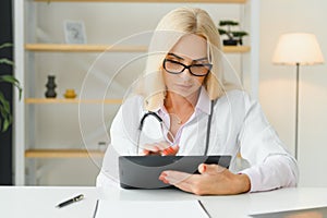 Portrait of middle age female doctor is wearing a white doctor& x27;s coat with a stethoscope around her neck. Smiling