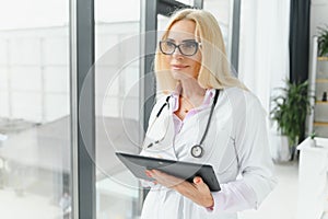 Portrait of middle age female doctor is wearing a white doctor& x27;s coat with a stethoscope around her neck. Smiling