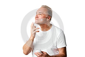 Portrait of middle aged, 45s man applying skin care cream on face against white studio background.