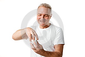 Portrait of middle aged, 45s man holding jar of skin care cream for face against white studio background.