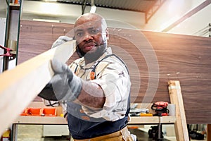 Portrait of middle-aged African carpenter wears apron, measuring and aiming wood plank, worker man makes wooden furniture in