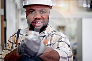 Portrait of middle-aged African carpenter wears white helmet, measuring and aiming wood plank, worker man make wooden furniture in