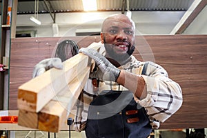 Portrait of middle-aged African craftsman carpenter wears apron, carrying wood planks, worker man makes wooden furniture in