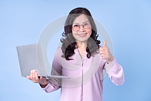 Portrait of middle aged Asian woman using laptop on blue background