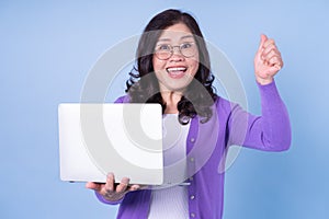 Portrait of middle aged Asian woman using laptop on blue background