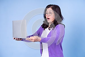 Portrait of middle aged Asian woman using laptop on blue background