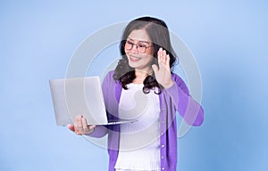 Portrait of middle aged Asian woman using laptop on blue background