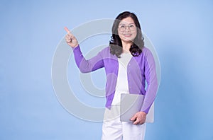 Portrait of middle aged Asian woman using laptop on blue background