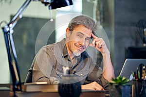 Portrait of middle aged bearded man at home. Older handsome guy smiling, looking at camera, working on laptop computer