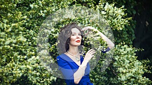 Portrait of a middle-aged brunette in a blue dress next to a blooming linden